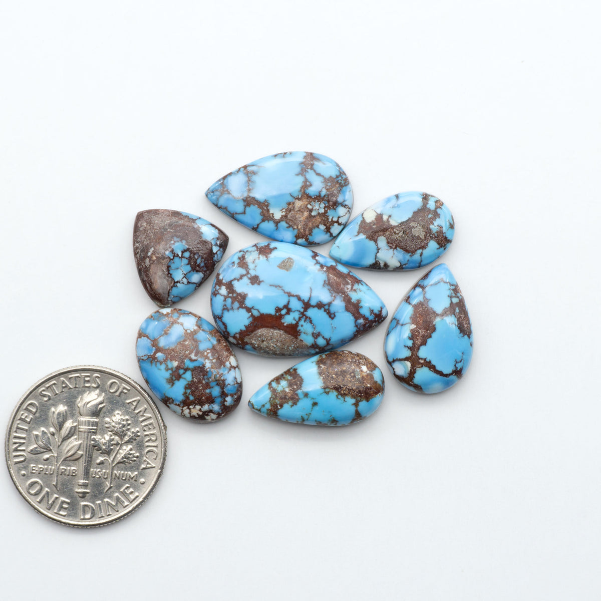 Golden Hills Turquoise cabochons, icy blue to lavender tones with chocolate matrix, polished stones on a white background with a US dime for scale