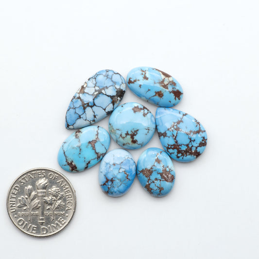 Golden Hills Turquoise cabochons, icy blue to lavender tones with chocolate matrix, polished stones on a white background with a US dime for scale