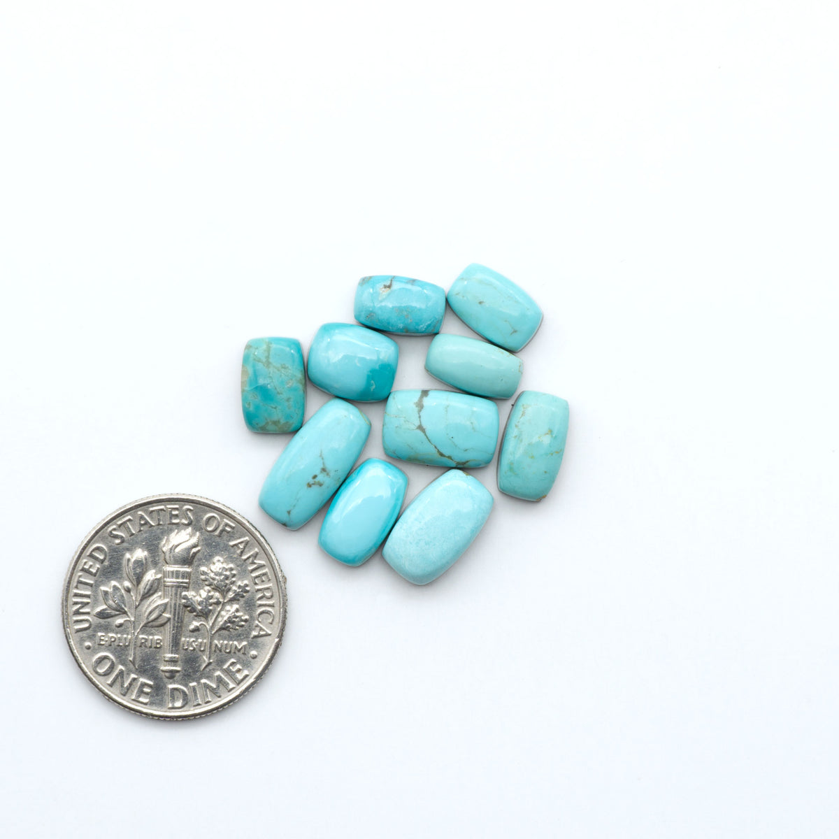 Kings Manassa Turquoise cabochons, polished green-blue gemstones with natural matrix on a white background with a US dime for scale